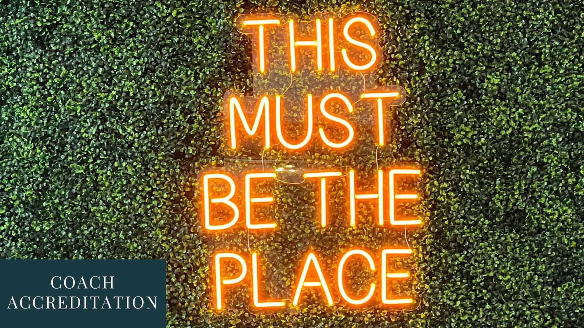 Quote: "This must be the place" in yellow neon letters against a leafy background with the words Coach Accreditation in a blue square